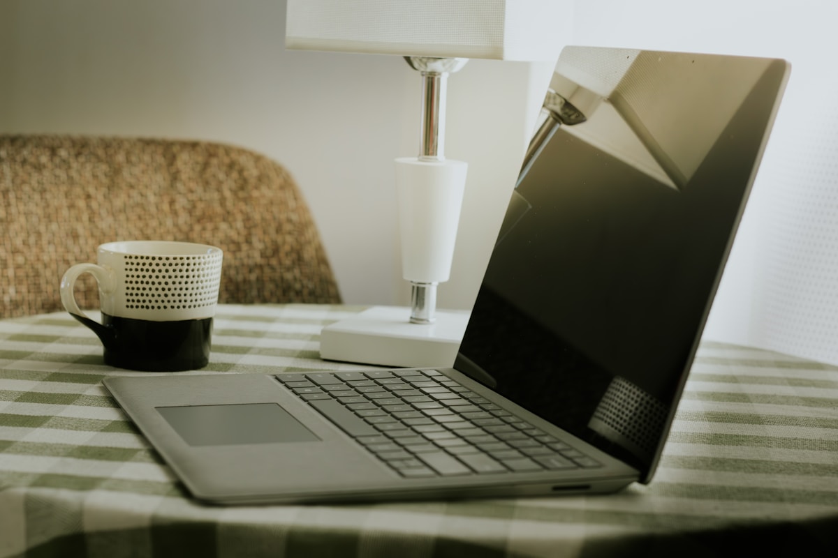 Ordinateur portable sur une table à carreaux, avec une tasse et une lampe.