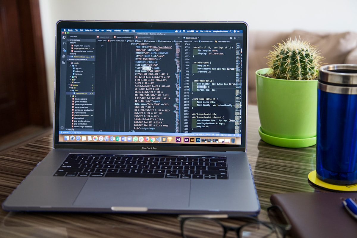 Ordinateur portable ouvert avec un code de programmation affiché à l'écran, entouré de plantes et d'accessoires de bureau.