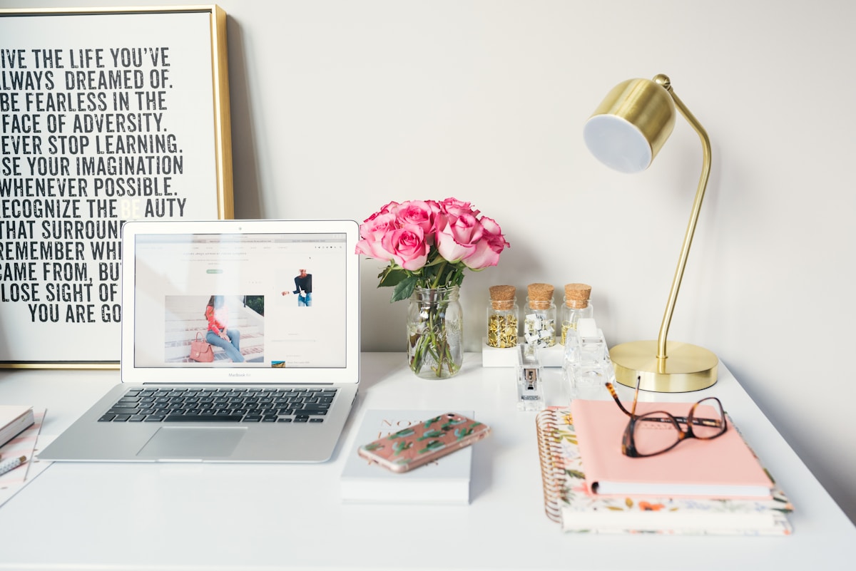 Bureau de travail élégant avec ordinateur portable, fleurs, lampe et accessoires.