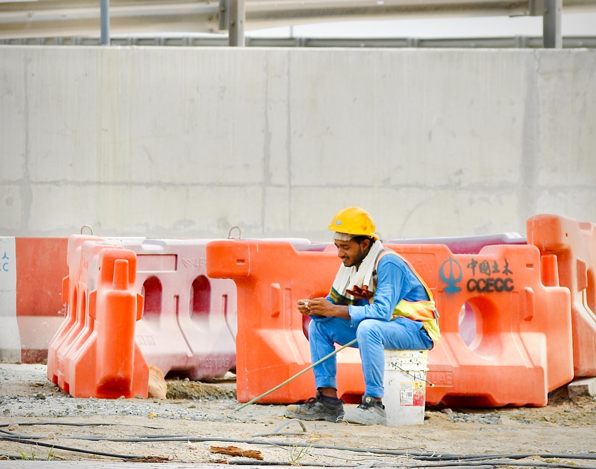 Ouvrier de construction assis sur des barrières de sécurité orange.