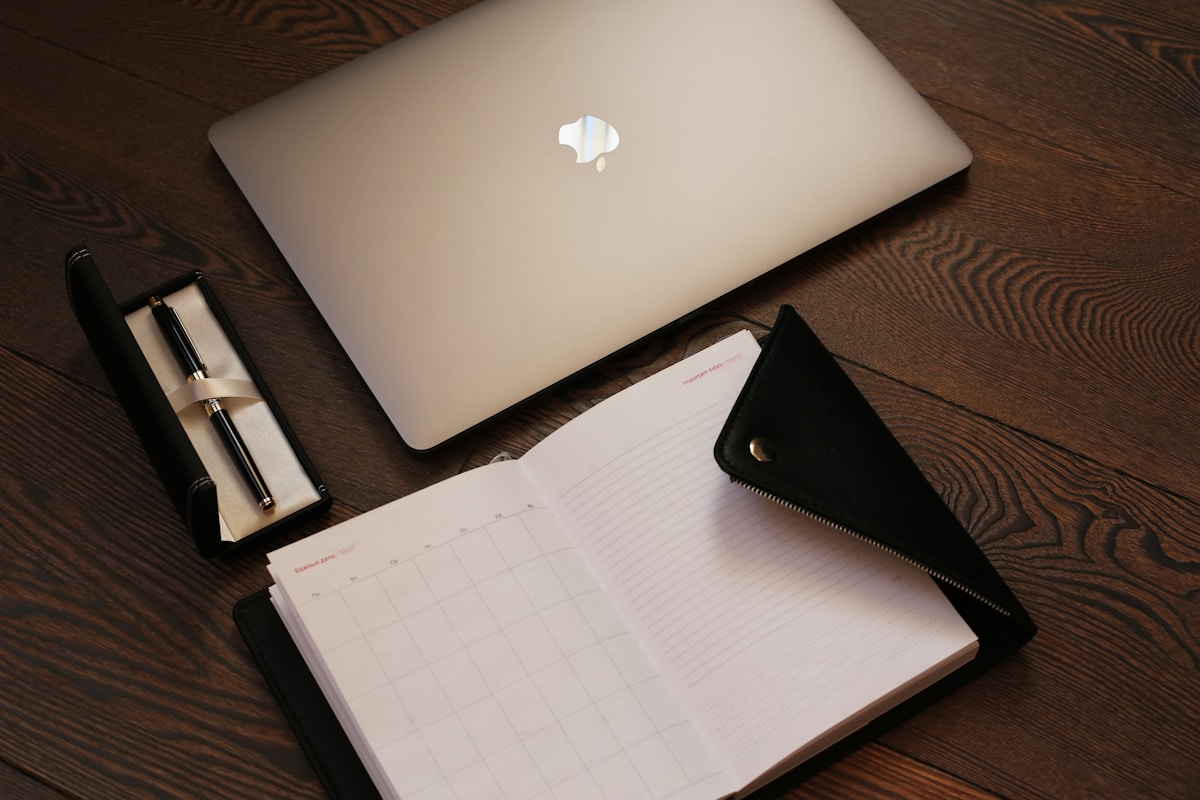 Ordinateur portable, agenda, stylo sur une table en bois.