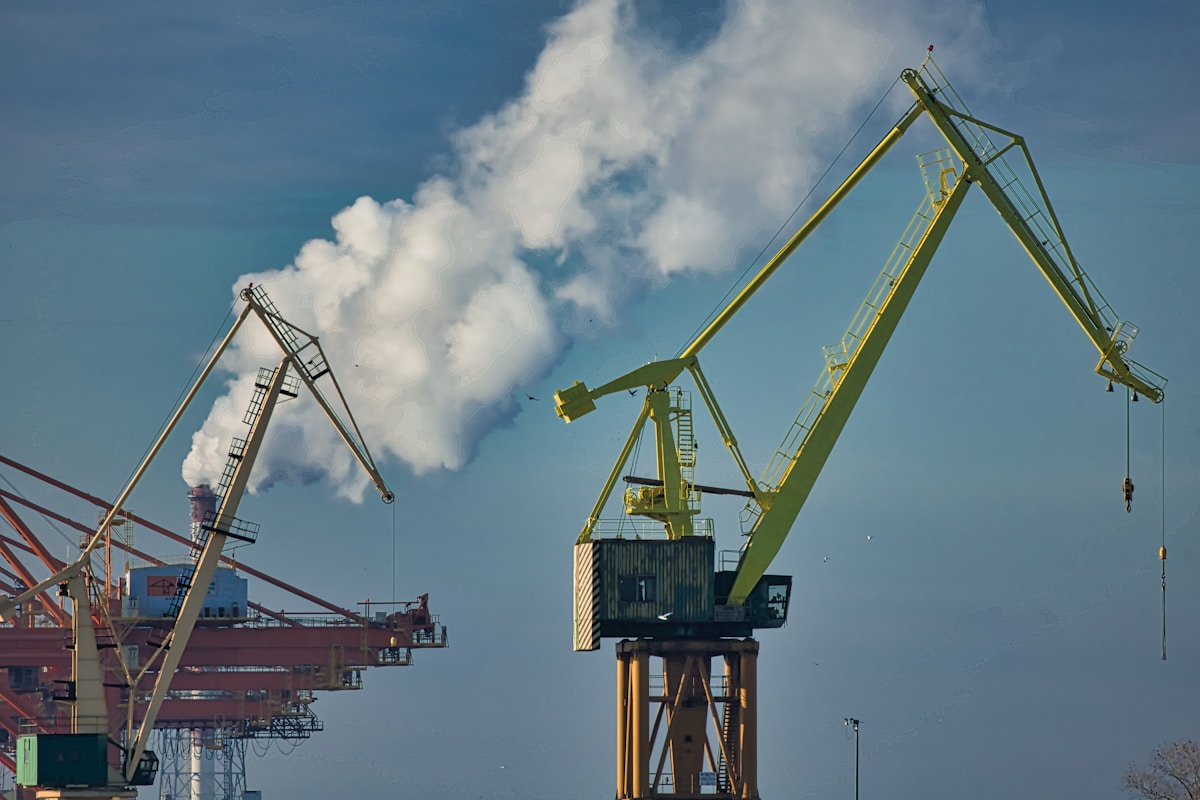 Grues portuaires jaunes soulevant des conteneurs sous un ciel nuageux.