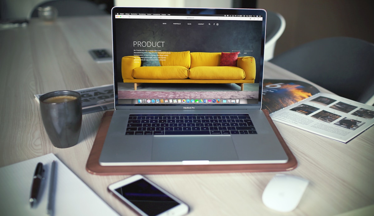 Ordinateur portable avec site web de produits, tasse de café, smartphone et photos sur un bureau en bois.