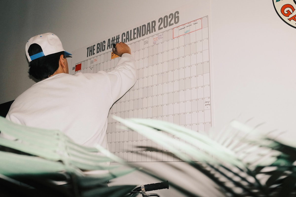 Homme en casquette examinant un grand calendrier mural 2026.