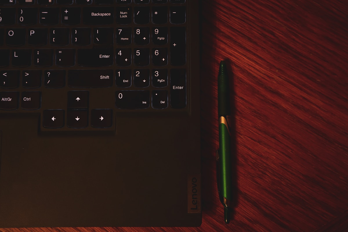 Clavier d'ordinateur noir avec un stylo vert sur un fond rouge foncé.